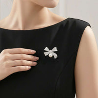 A close-up of a woman wearing a black sleeveless dress ,wearing a silver bow-shaped brooch with a freshwater pearl.