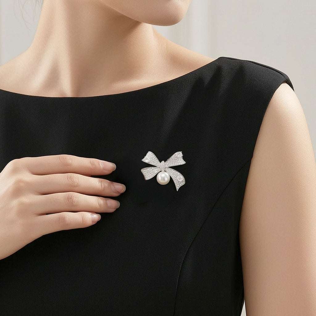 A close-up of a woman wearing a black sleeveless dress ,wearing a silver bow-shaped brooch with a freshwater pearl.