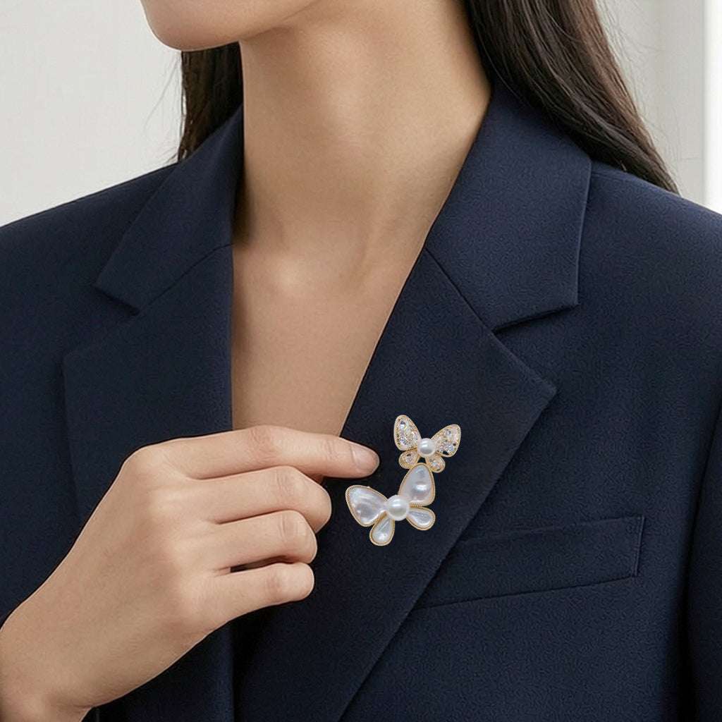 A close-up of a woman wearing a navy blazer and touching a butterfly-shaped pearl brooch pinned to her lapel.