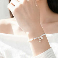 A delicate bracelet worn on a woman's wrist, featuring freshwater pearls and a small rose gold flower charm, shown in a bright, softly lit lifestyle setting.