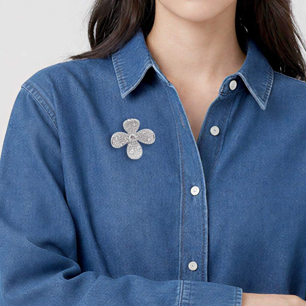 A close-up of a person wearing a blue denim button-up shirt with a cubic zirconia flower-shaped brooch pinned to the chest.