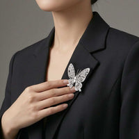 A close-up of a woman wearing a black blazer and touching a silver butterfly-shaped brooch pinned to her blazer lapel。