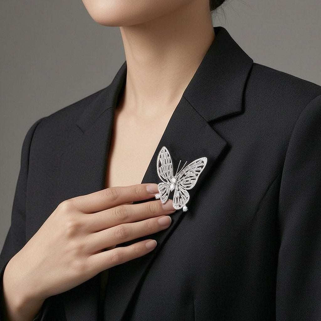 A close-up of a woman wearing a black blazer and touching a silver butterfly-shaped brooch pinned to her blazer lapel。