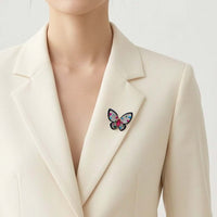 A close-up of a model wearing a cream-colored blazer with a colorful butterfly brooch pinned to the lapel.