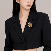 A close-up of a model wearing a black cropped blazer with a colorful circular pin brooch on the lapel.
