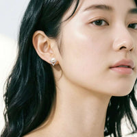A close-up of a woman's ear wearing a small silver triangular stud earring with a freshwater pearl center.