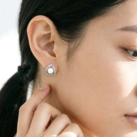A close-up of a woman's ear wearing a triangular stud earring with a freshwater pearl surrounded by a cubic zirconia.