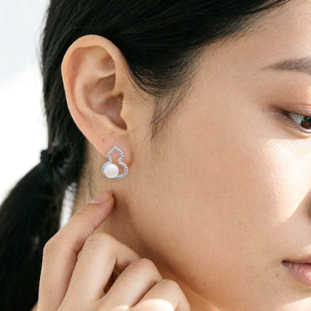 A close-up of a woman's ear wearing a silver hulu-shaped stud earring with a freshwater pearl center and small cubic zirconia