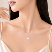 A close-up of a woman wearing a delicate silver-tone butterfly necklace with a mother-of-pearl butterfly pendant, paired with a cream satin camisole.