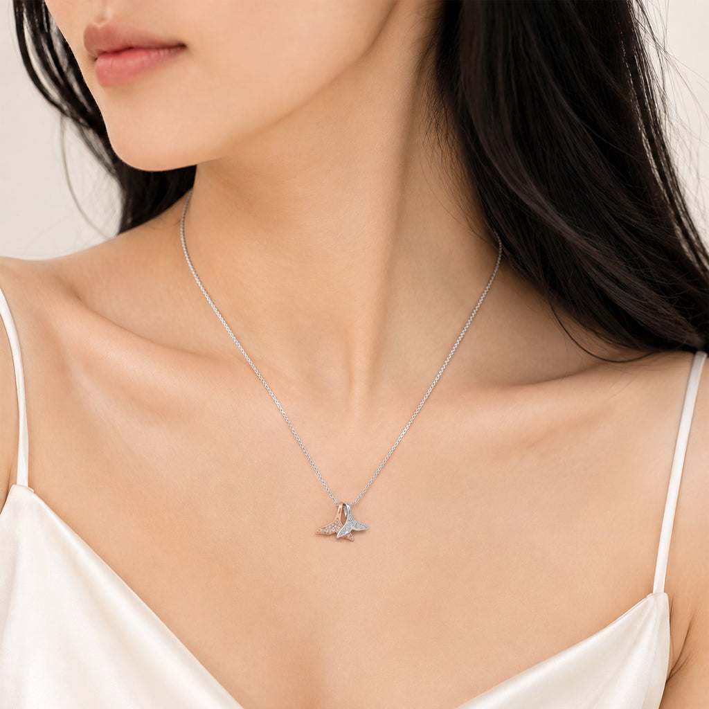 A close-up of a woman wearing a delicate mermaid tail pendant necklace  styled with a white satin camisole.