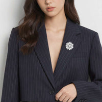 A close-up of a woman wearing a dark navy pinstripe blazer with a cubic zirconia flower-shaped brooch pinned to the lapel.