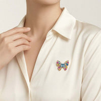 A close-up of a person wearing a cream satin collared shirt and a small butterfly-shaped brooch embellished with multicolored stones on the chest.