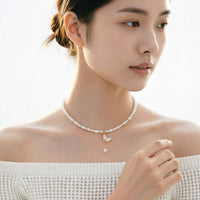 A woman wearing a delicate pearl necklace with a gold-toned butterfly pendant and a single pearl drop.