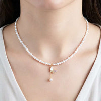A close-up of a model wearing a delicate white pearl necklace with a gold butterfly pendant featuring a dangling pearl.