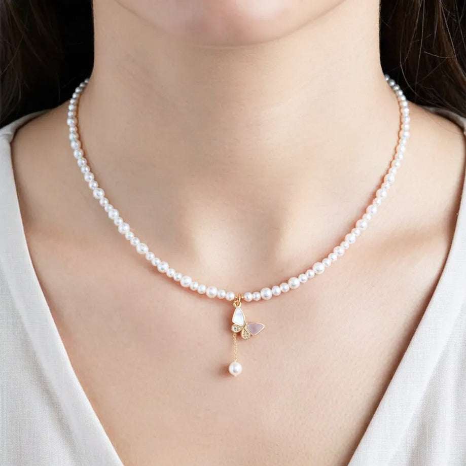 A close-up of a model wearing a delicate white pearl necklace with a gold butterfly pendant featuring a dangling pearl.