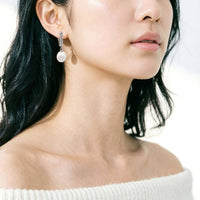 A close-up of a woman wearing a silver drop earring with a freshwater pearl.