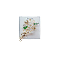Floral Cubic Zirconia Brooch with white petals, green leaves, gold-tone stems, sparkling stones and a bow detail.