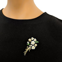 Cubic Zirconia Brooch featuring a gold-tone floral spray, white enamel flowers, sparkling stones, and green leaves.