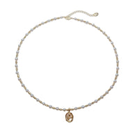 Freshwater Pearl Necklace with small round white pearls, gold-plated beads, and an oval gold pendant on a wire choker.
