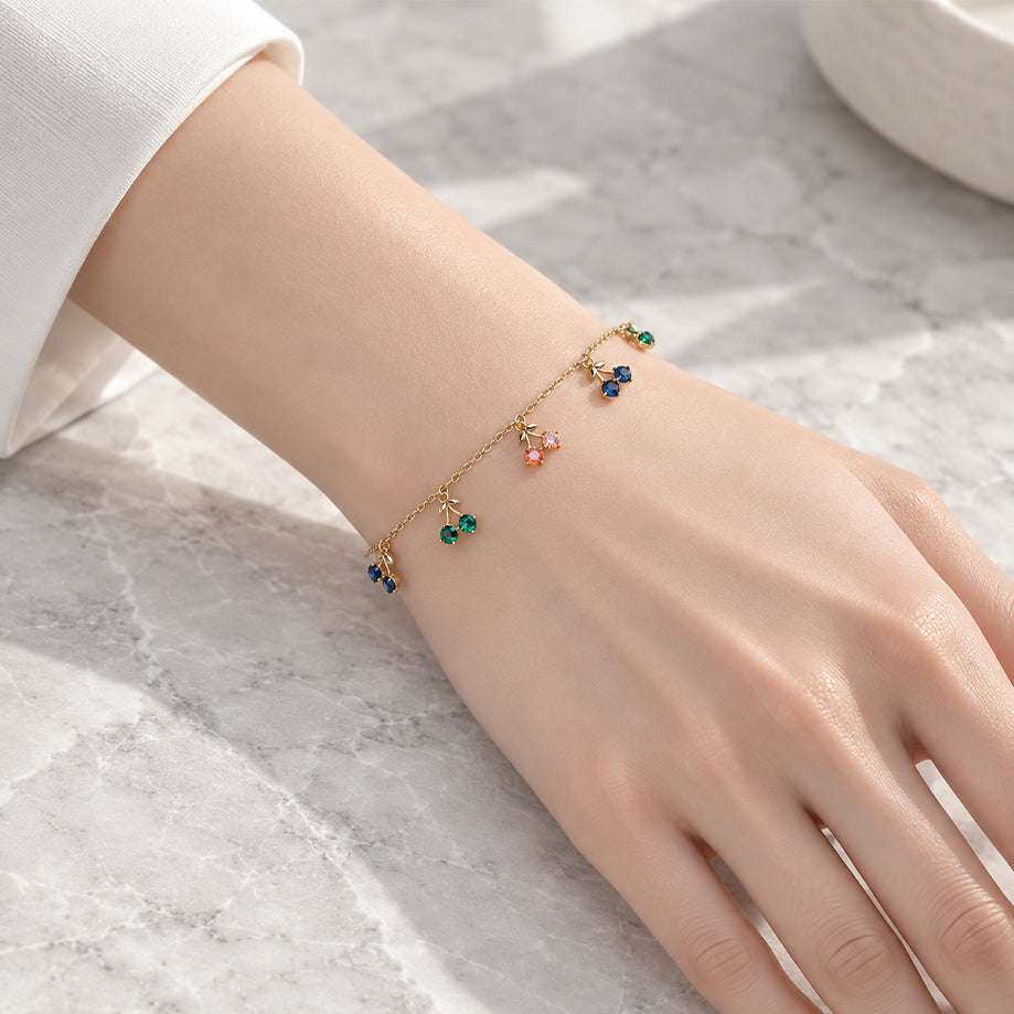 Gold-tone cherry bracelet with a fine chain and dangling multicolour cherry charms set with sparkling stones.