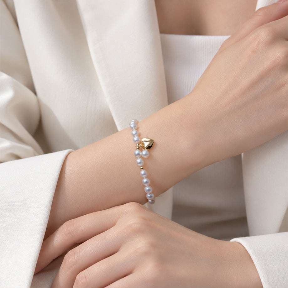 Freshwater Pearl Bracelet with lustrous white pearls, tiny gold spacer beads and a gold heart-shaped centre charm on a delicate strand.