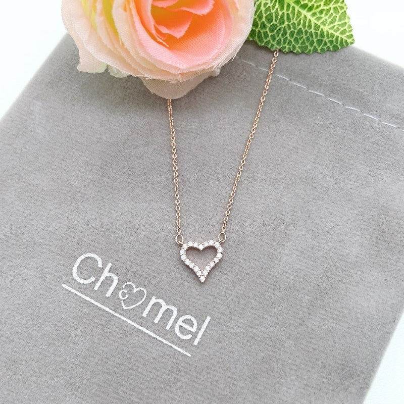Heart shaped cubic zirconia pendant necklace with rose gold plating on grey pouch next to pink rose